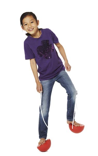 Kind spielt mit roten Stelzen aus Kunststoff, trägt lila Shirt und Jeans, weißer Hintergrund.