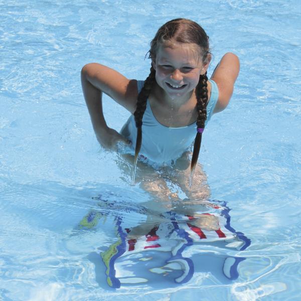 Mädchen mit Zöpfen spielt lachend im klaren Wasser eines Schwimmbeckens.