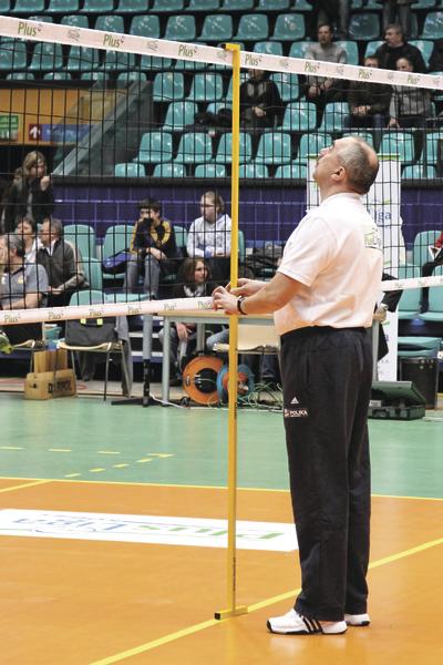 Schiedsrichter misst die Netzhöhe bei einem Volleyballspiel in der Halle.