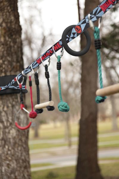 Outdoor-Kletter- und Turngerät mit verschiedenen Griffen und Seilen zwischen Bäumen.