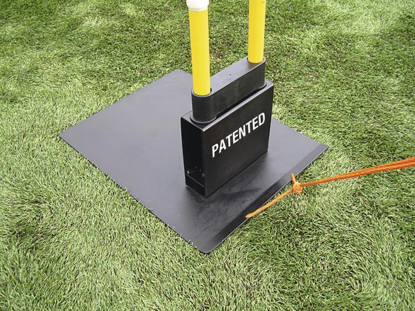 Schwarze patentierte Bodenhalterung mit gelben Stangen auf grünem Rasen, gesichert mit orangefarbener Schnur.