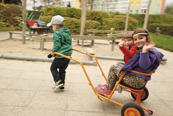 Kinder spielen draußen, ein Junge zieht zwei Mädchen auf einem Dreirad im Park.