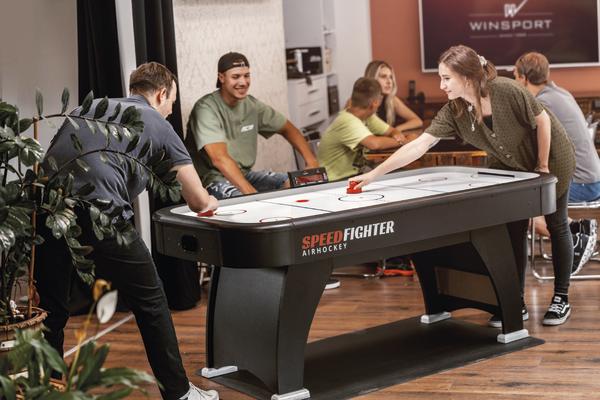 Junge Erwachsene spielen Airhockey an einem Speedfighter Tisch in einem modernen Freizeitraum.