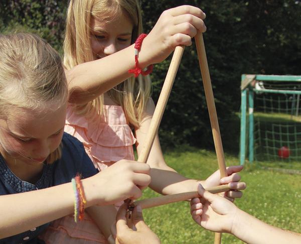 Zwei Mädchen spielen draußen mit einem Holz-Dreiecksspiel im Garten bei Sonnenschein.
