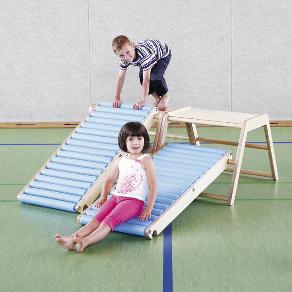 Kind spielt auf blauer Rutsche aus Holz in Turnhalle, Junge klettert, Mädchen sitzt unten.