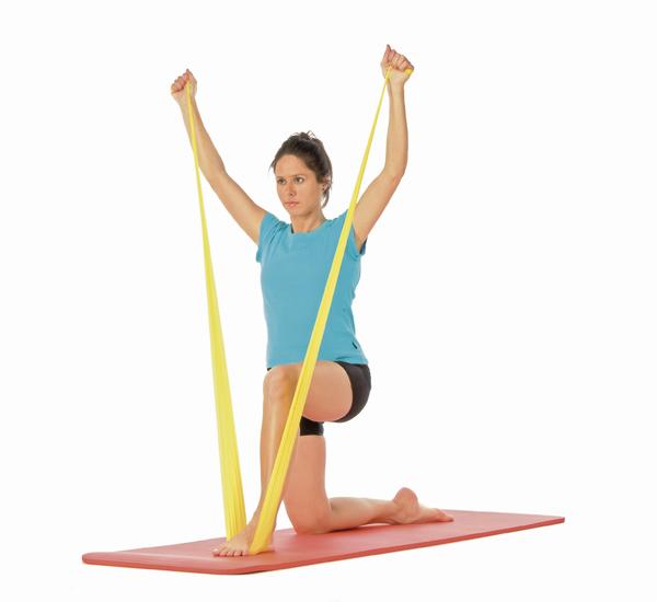 Frau macht Widerstandsband-Übung auf Yogamatte zur Kräftigung der Arme und Schultern.