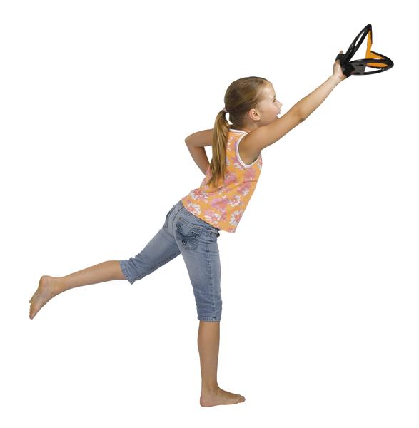 Mädchen in Jeans und Top fängt Frisbee im Sprung vor weißem Hintergrund.