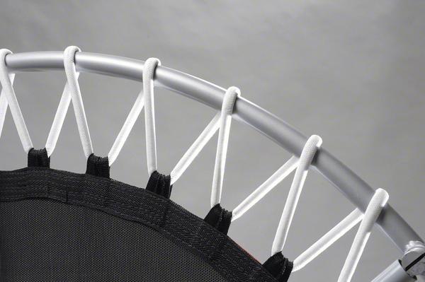 Nahaufnahme eines Trampolins mit elastischen Seilen und Metallrahmen vor grauem Hintergrund.