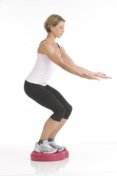 Frau macht Kniebeuge auf Balancekissen für Stabilität und Gleichgewichtstraining.