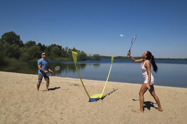 Paar spielt Badminton am Sandstrand eines Sees bei sonnigem Wetter.