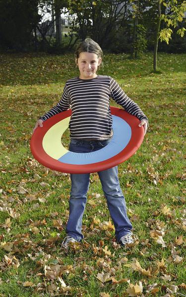 Kind spielt draußen mit buntem Wurfring im Herbst auf grünem Rasen.