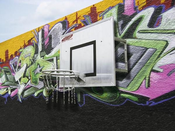 Basketballkorb mit Metallnetz an bunter Graffiti-Wand im Freien.