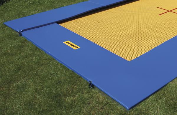 Bodentrampolin mit gelber Sprungfläche und blauem Rand auf grünem Rasen