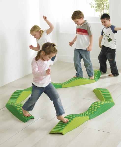 Kinder balancieren spielerisch auf grünem Balancierpfad im hellen Raum.