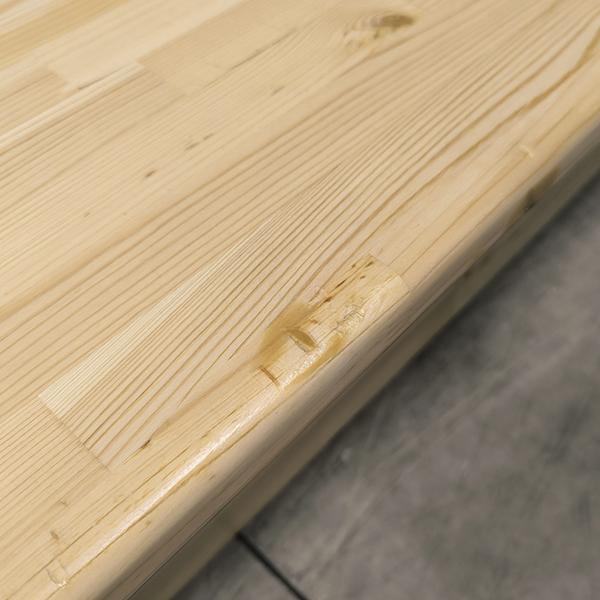 Nahaufnahme einer Holzplatte mit kleiner Delle und sichtbarer Maserung auf grauem Boden.