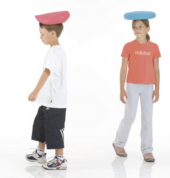 Junge und Mädchen balancieren farbige Kissen auf dem Kopf, sportliche Kleidung, weißer Hintergrund.