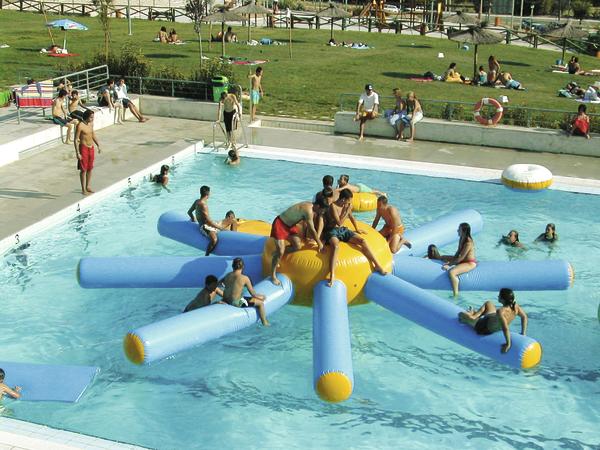 Menschen spielen auf einem blauen und gelben Wasser-Spielgerät in einem Schwimmbad.