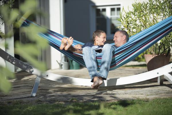 Vater und Sohn entspannen gemeinsam in bunter Hängematte im Garten an sonnigem Tag.