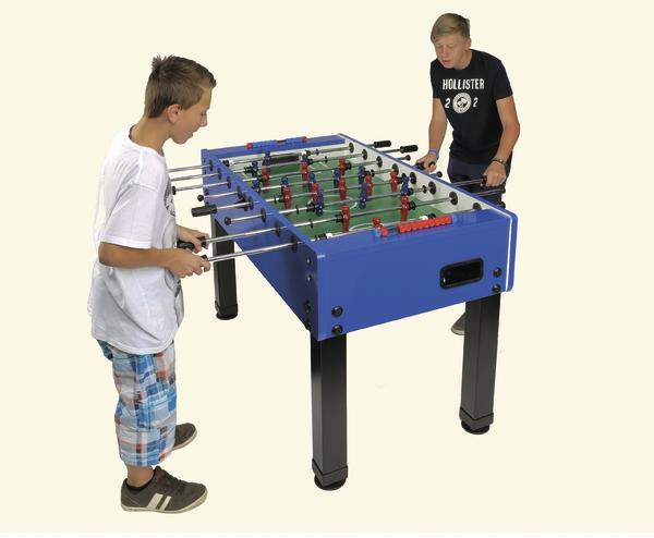 Zwei Jungen spielen Tischkicker an einem blauen Kicker-Tisch vor hellem Hintergrund.