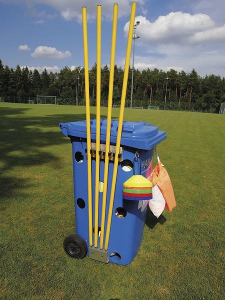 Blaue Spieltonne mit gelben Stangen und Markierungshütchen auf Fußballfeld bei Sonnenschein.