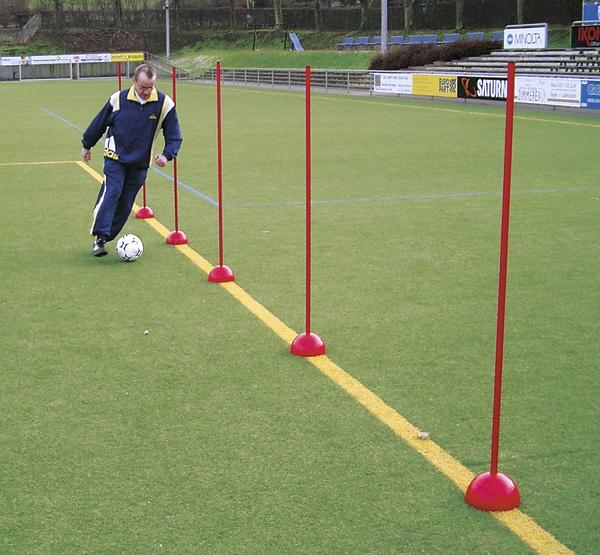 Mann trainiert Fußball-Dribbling auf Kunstrasen mit roten Slalomstangen.