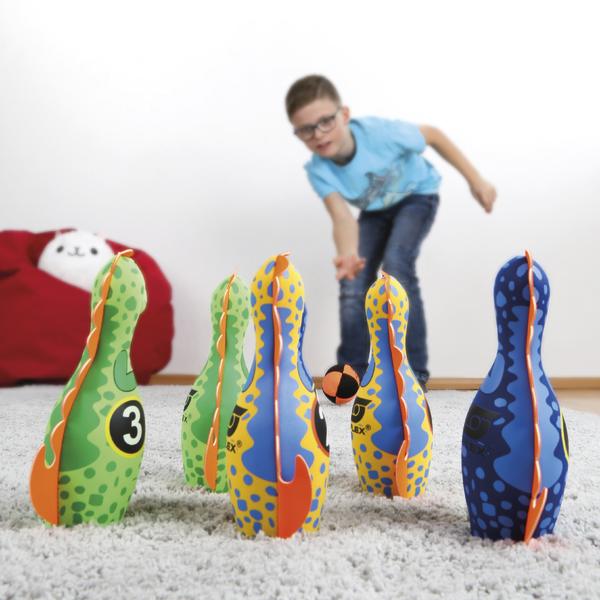 Kind spielt mit bunten Indoor-Bowling-Pins und wirft Ball auf Teppichboden.