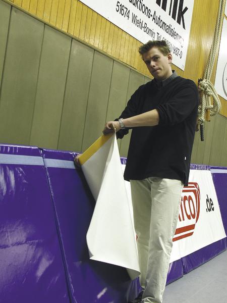 Mann bringt Werbebanner an einer Sporthallenwand an, um Werbung sichtbar zu machen.