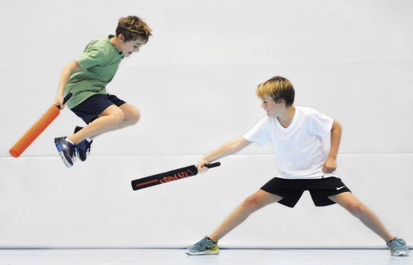 Zwei Jungen kämpfen spielerisch mit Schaumstoffstäben, einer springt in die Luft.