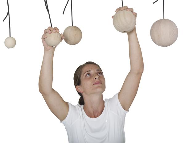 Frau in weißem Shirt greift nach hängenden Holz-Kugeln vor weißem Hintergrund.