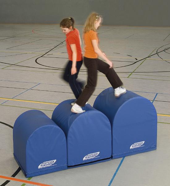 Zwei Mädchen balancieren auf blauen Sportgeräten in einer Turnhalle.