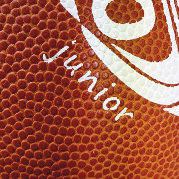 Detailaufnahme eines braunen SPORTCO Junior Gummi-Footballs mit stark genoppter Oberfläche und weißem Logo-Aufdruck im klassischen American-Football-Design