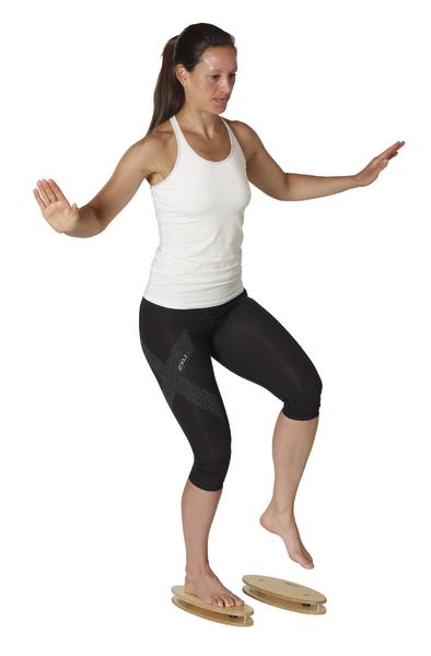 Frau trainiert Gleichgewicht mit Balance-Boards in Sportbekleidung vor weißem Hintergrund.