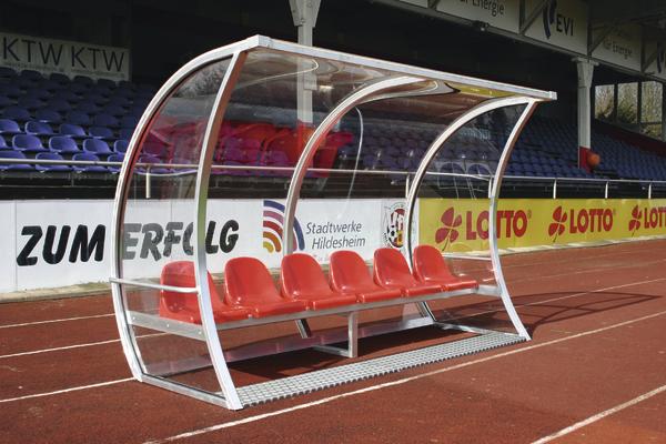 Rote Sitzbank mit Überdachung für Spieler auf einer Sportplatz-Seitenlinie.