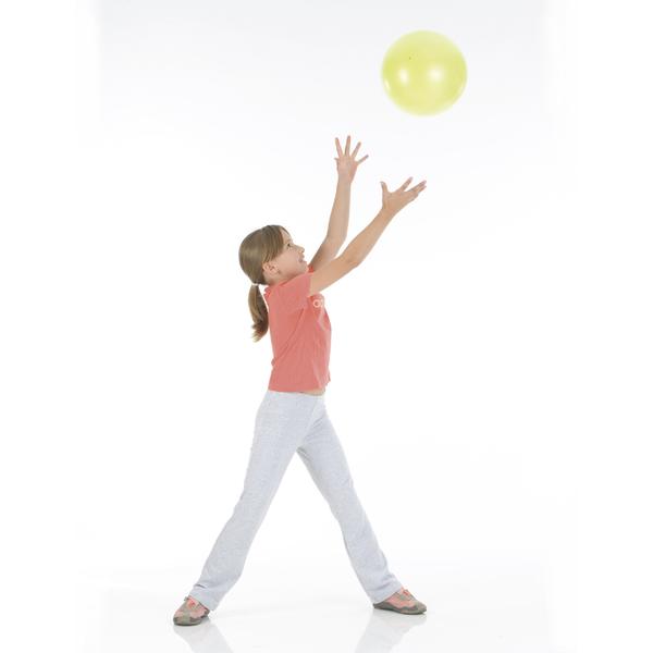 Mädchen in Sportkleidung fängt gelben Gymnastikball im weißen Studio.