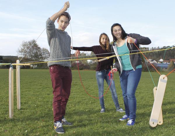 Drei Jugendliche spielen draußen mit einem Seilspiel auf einer grünen Wiese bei klarem Himmel.