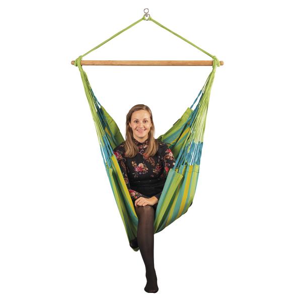 Frau sitzt entspannt in grün-blau gestrechter Hängematte mit Holzquerstab vor weißem Hintergrund.
