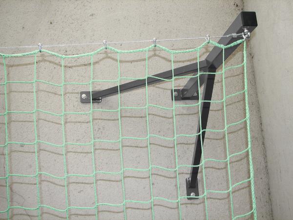 Befestigung eines grünen Schutznetzes an einer Wand mit schwarzem Metallhalter.