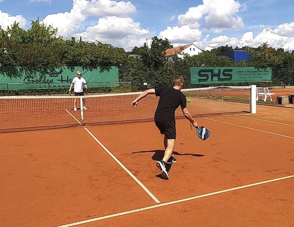 Zwei Männer spielen Padel auf einem Sandplatz bei sonnigem Wetter.