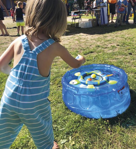 Kind spielt im Freien mit aufblasbarem Wasserspielzeug auf Gras bei sonnigem Wetter.