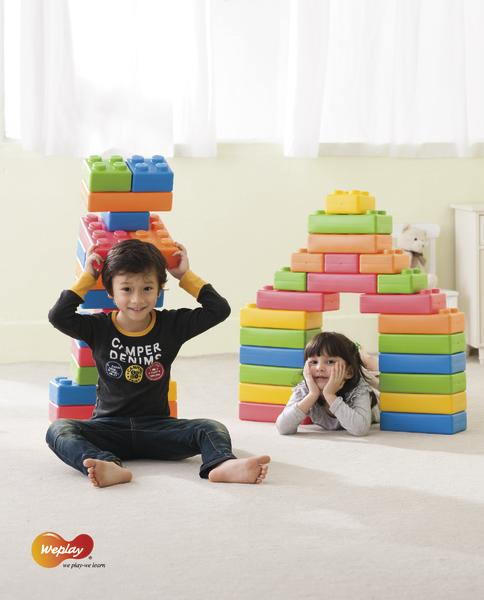 Kind spielt mit bunten Bausteinen, Mädchen liegt in einem Tor aus großen Spielklötzen.
