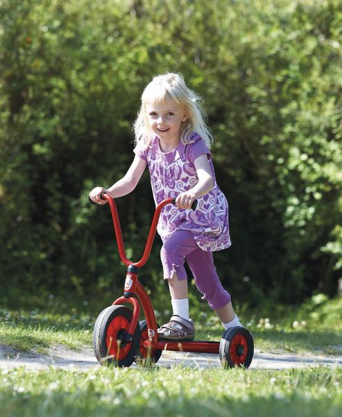 Kleines Mädchen fährt fröhlich roten Dreiradroller im Park bei Sonnenschein.