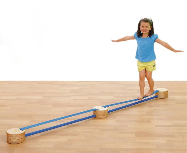 Mädchen balanciert auf einem blauen Slackline-Band in einem hellen Raum mit Holzboden.