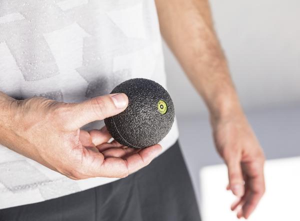 Mann hält schwarzen Massageball zur Selbstmassage und Muskelentspannung in der Hand.