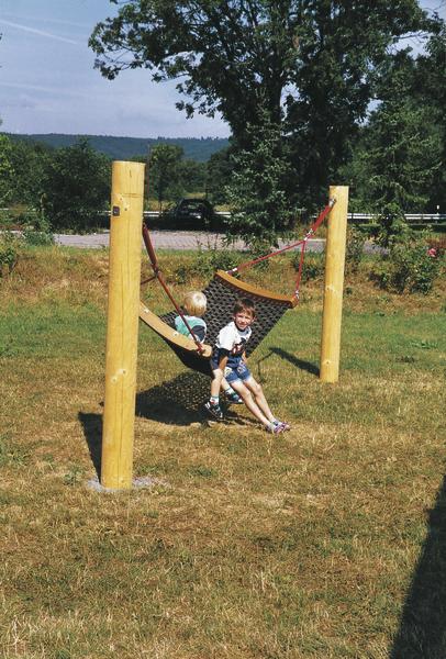Kinder spielen auf einer Hängematte zwischen zwei Holzpfosten im Garten.