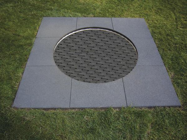 Runde Metallgitter-Abdeckung in quadratischem Steinrahmen auf Grasfläche.