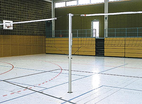 Leerer Volleyballplatz in einer hellen Sporthalle mit Netz und Basketballkorb.
