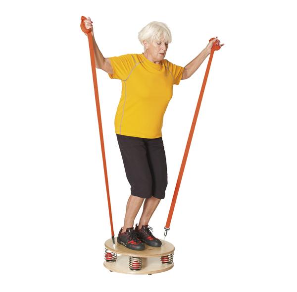 Ältere Frau trainiert Gleichgewicht und Kraft mit Feder-Balance-Board und Widerstandsbändern.