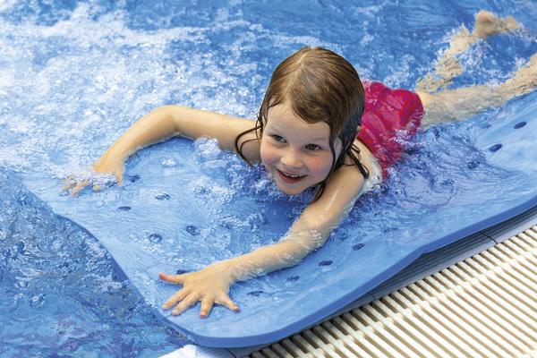 Kind im roten Badeanzug lernt Schwimmen mit Schwimmbrett im Hallenbad.