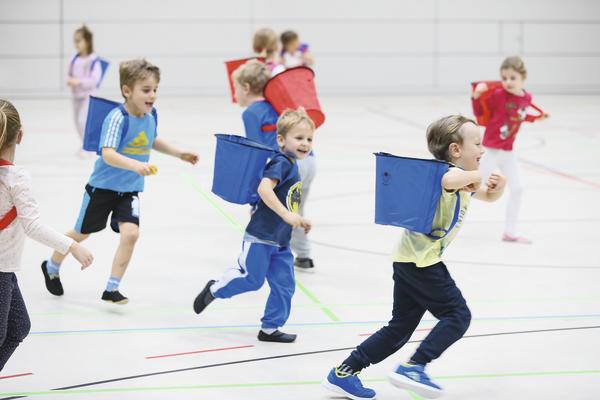 Kinder spielen Fangspiel mit bunten Fangnetzen in einer hellen Sporthalle.