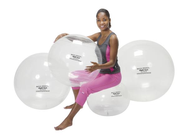Frau in Sportkleidung sitzt auf großem transparentem Gymnastikball, umgeben von weiteren Bällen.
